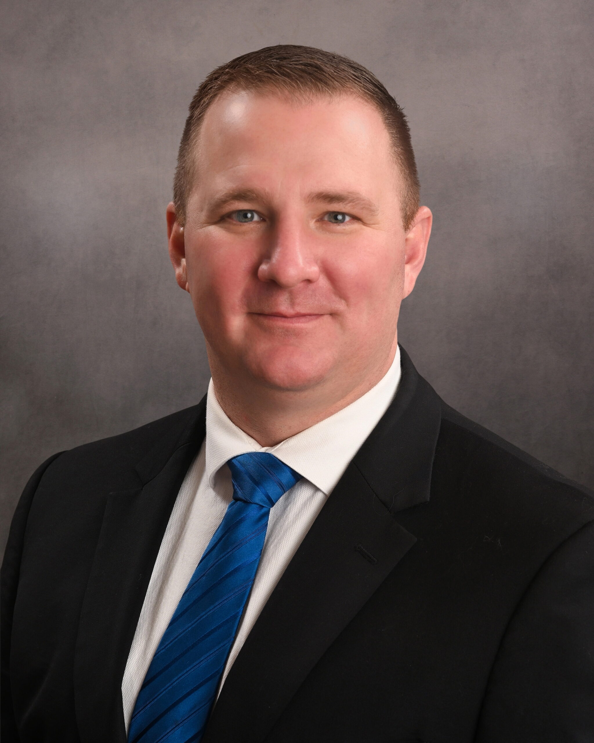 Professional man in suit and blue tie against a gray background.